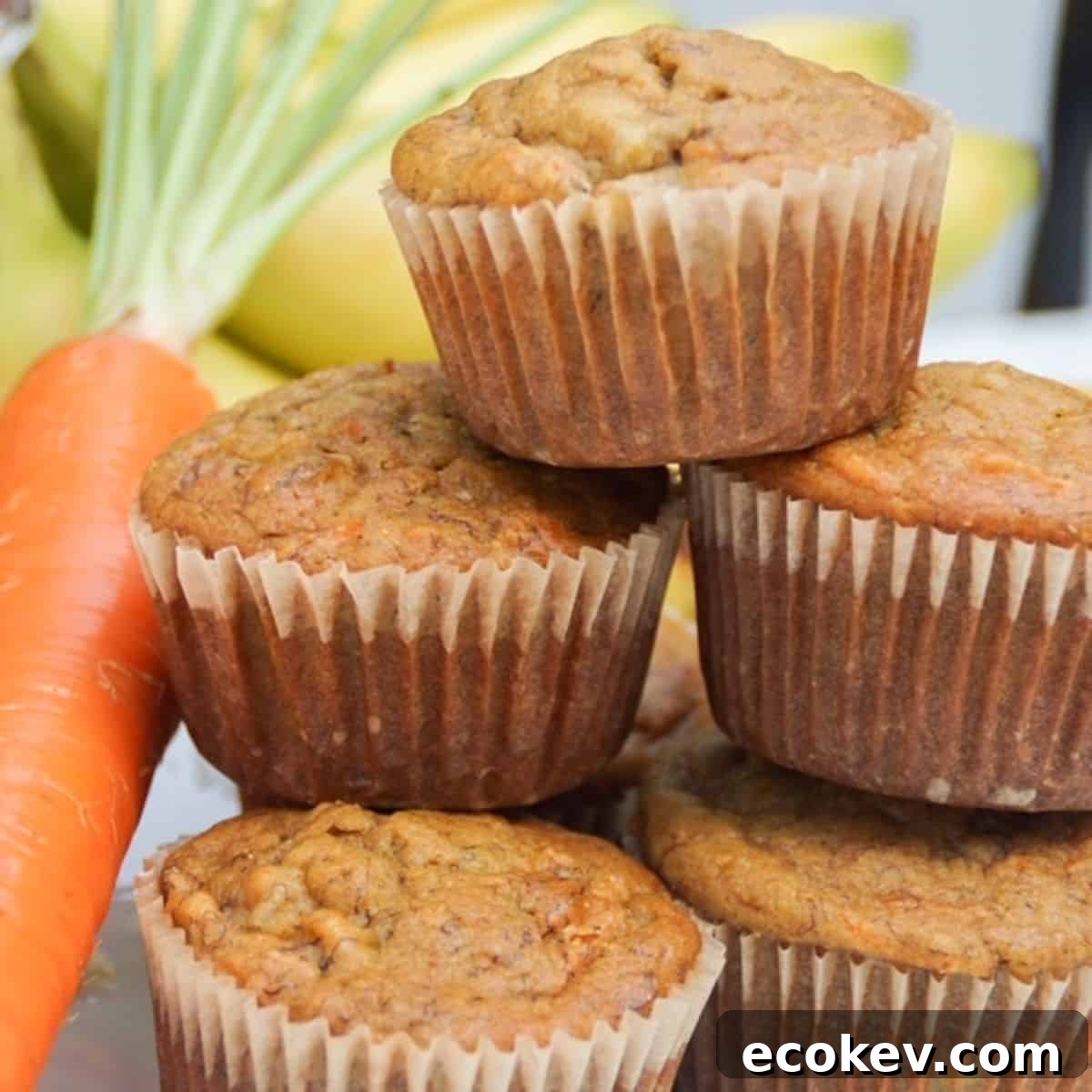stack of banana carrot muffins with a carrot on the side and bananas in the background