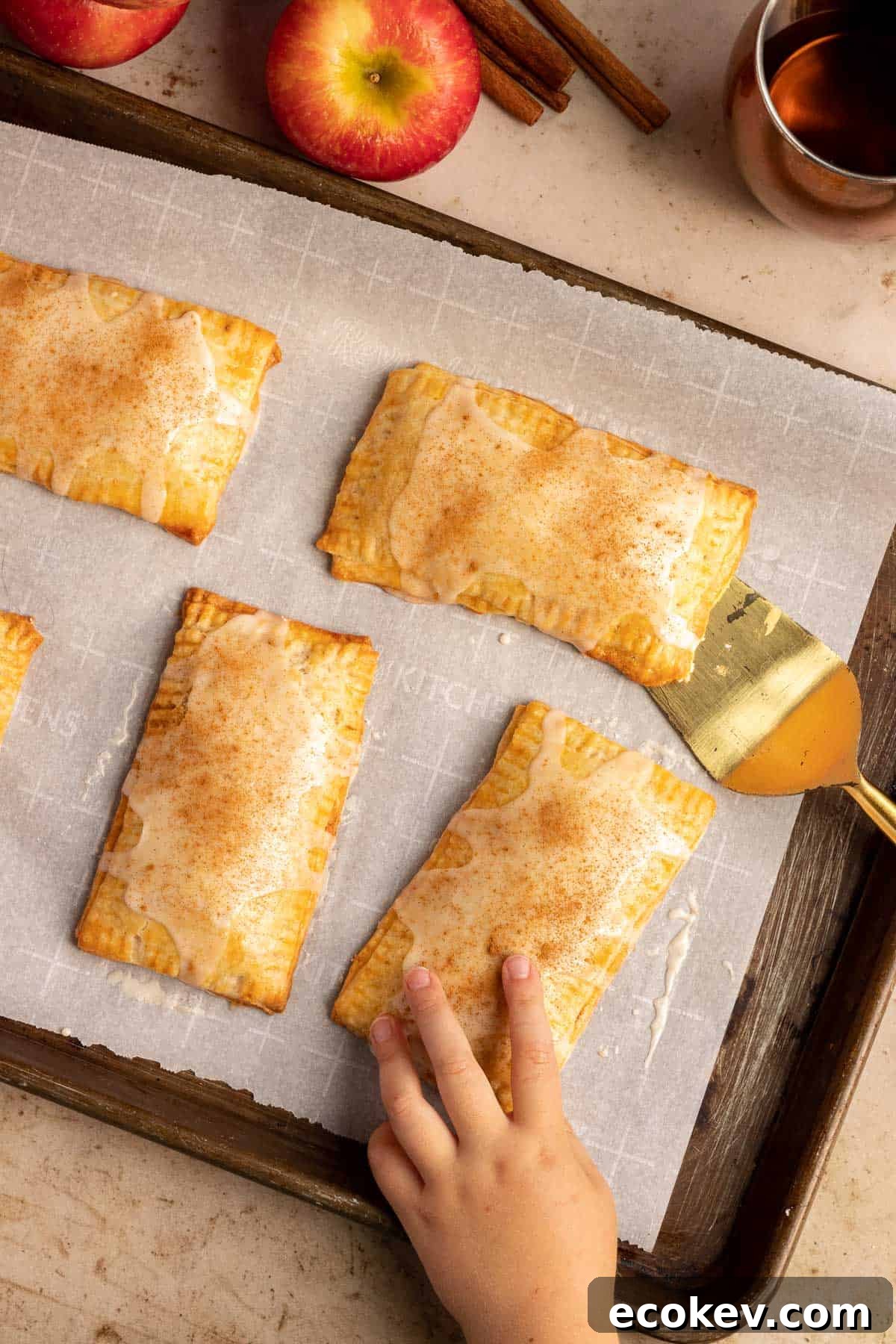 cinnamon apple pop tarts on a baking sheet with a child's hand grabbing one from the sheet