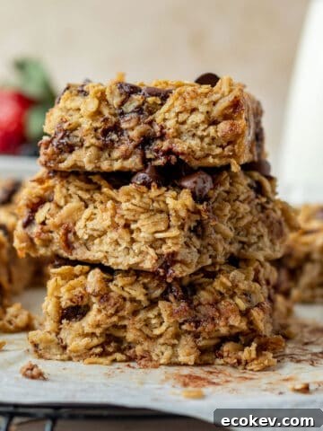 a stack of three chocolate chip baked oatmeal squares with a bowl of berries and carafe of milk in the background