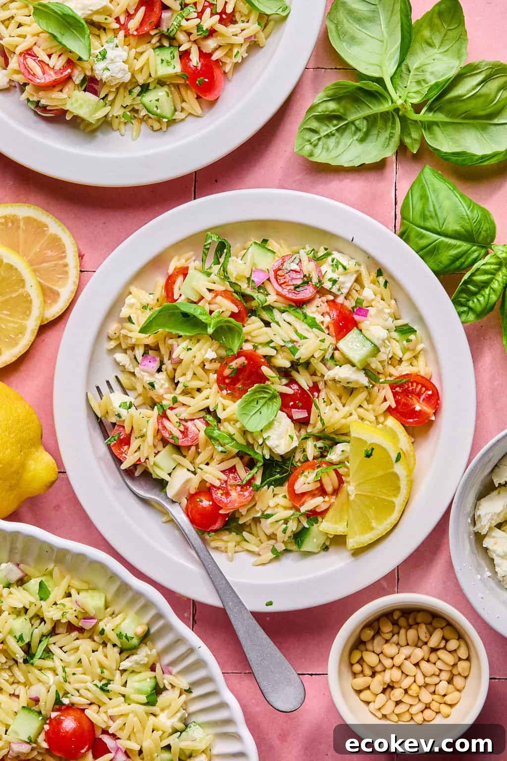 Overhead view of a lemon basil orzo salad with cherry tomatoes, cucumbers, feta cheese, red onions, and fresh basil, garnished with lemon wedges.