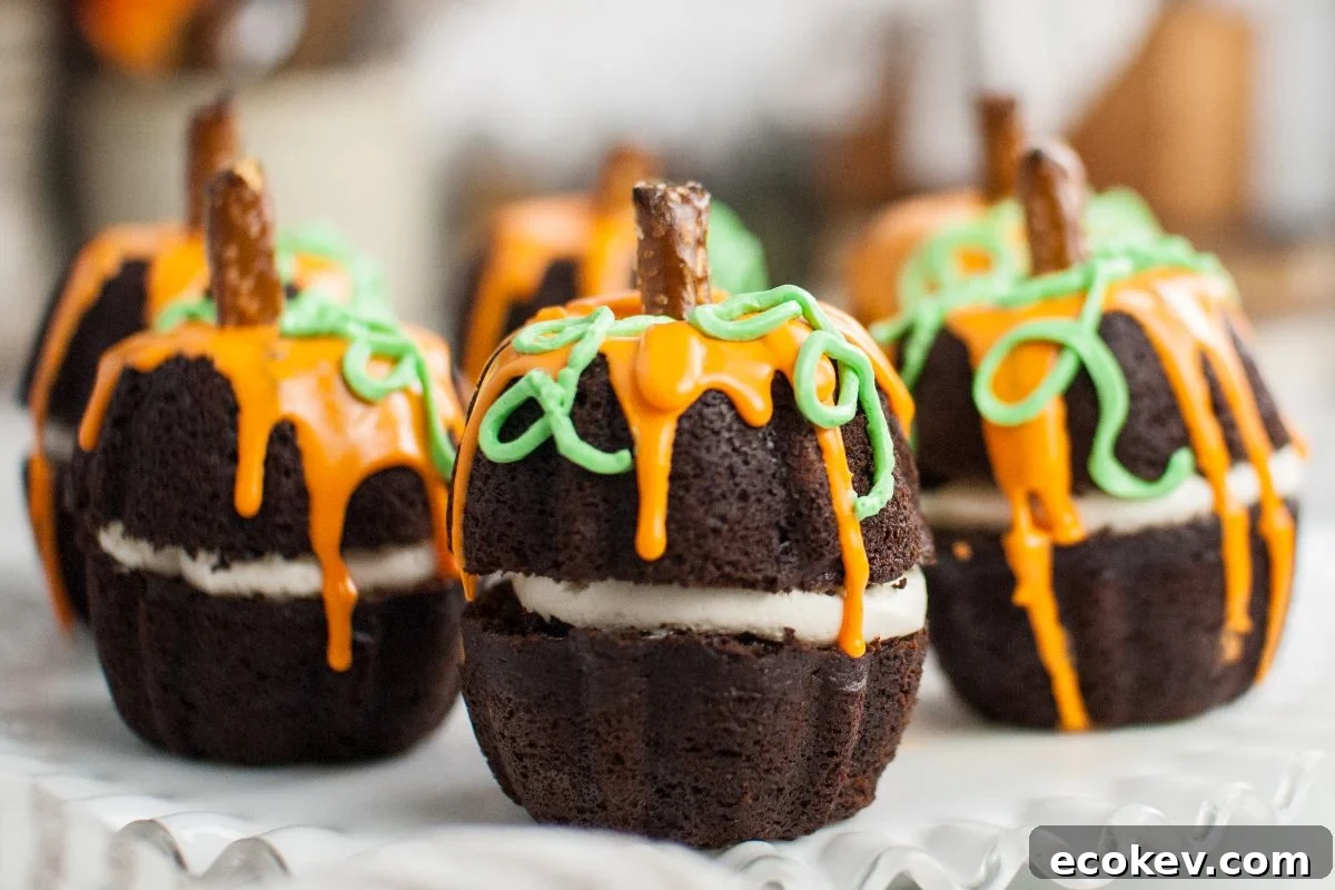Chocolate cupcakes decorated as pumpkins with orange and green icing and a pretzel stem—perfect mini Halloween pumpkin cakes for your spooky celebration.