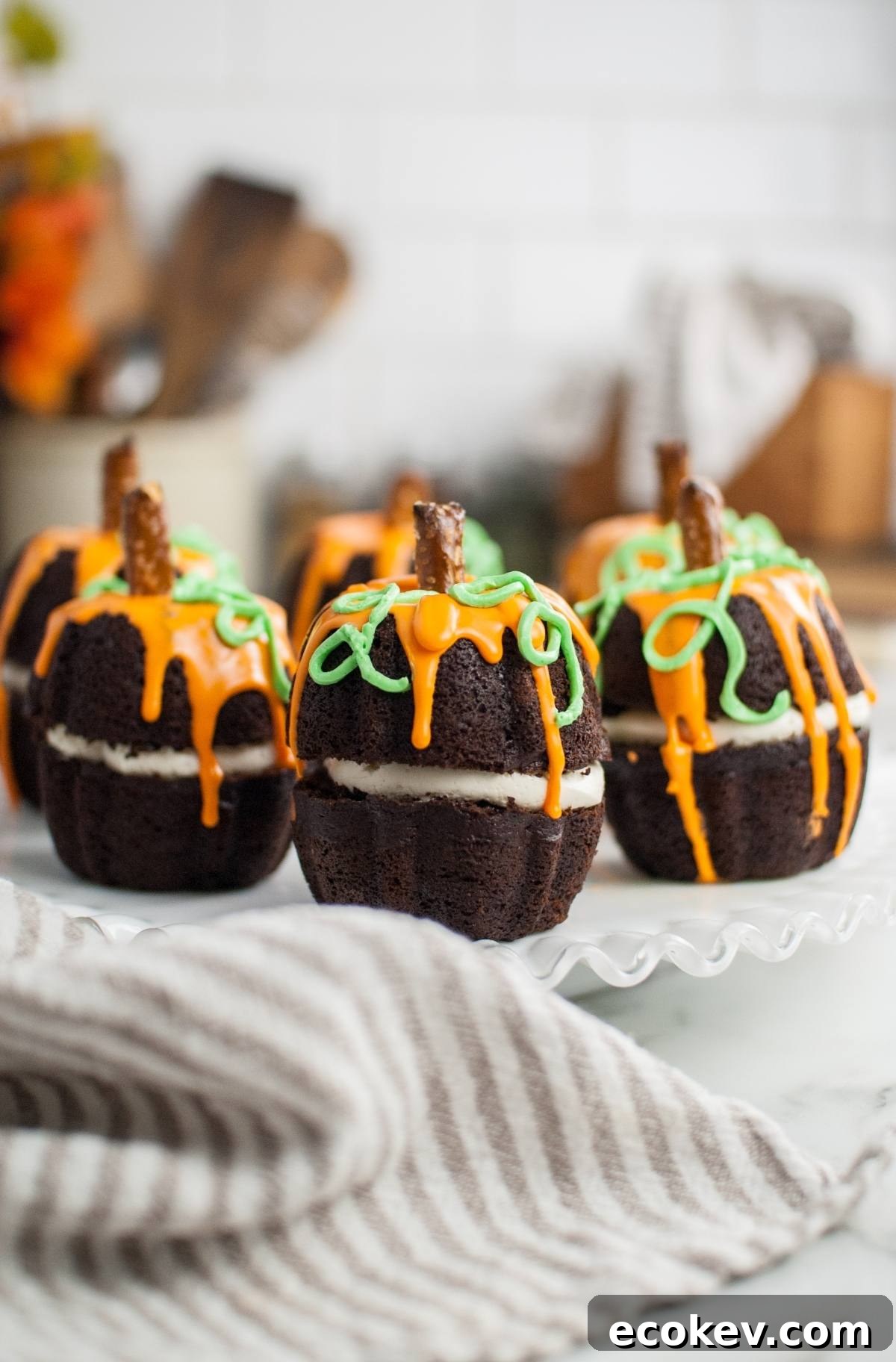 Chocolate pumpkin-shaped cakes with orange and green icing, topped with pretzel sticks, make the perfect Halloween pumpkin cakes for your next Thanksgiving or Halloween dessert display.