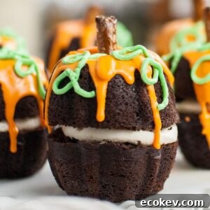 Chocolate cupcakes decorated like pumpkins with orange icing, green vines, and pretzel stick stems—perfect as a Thanksgiving or Halloween dessert or for learning how to make a pumpkin shaped cake.