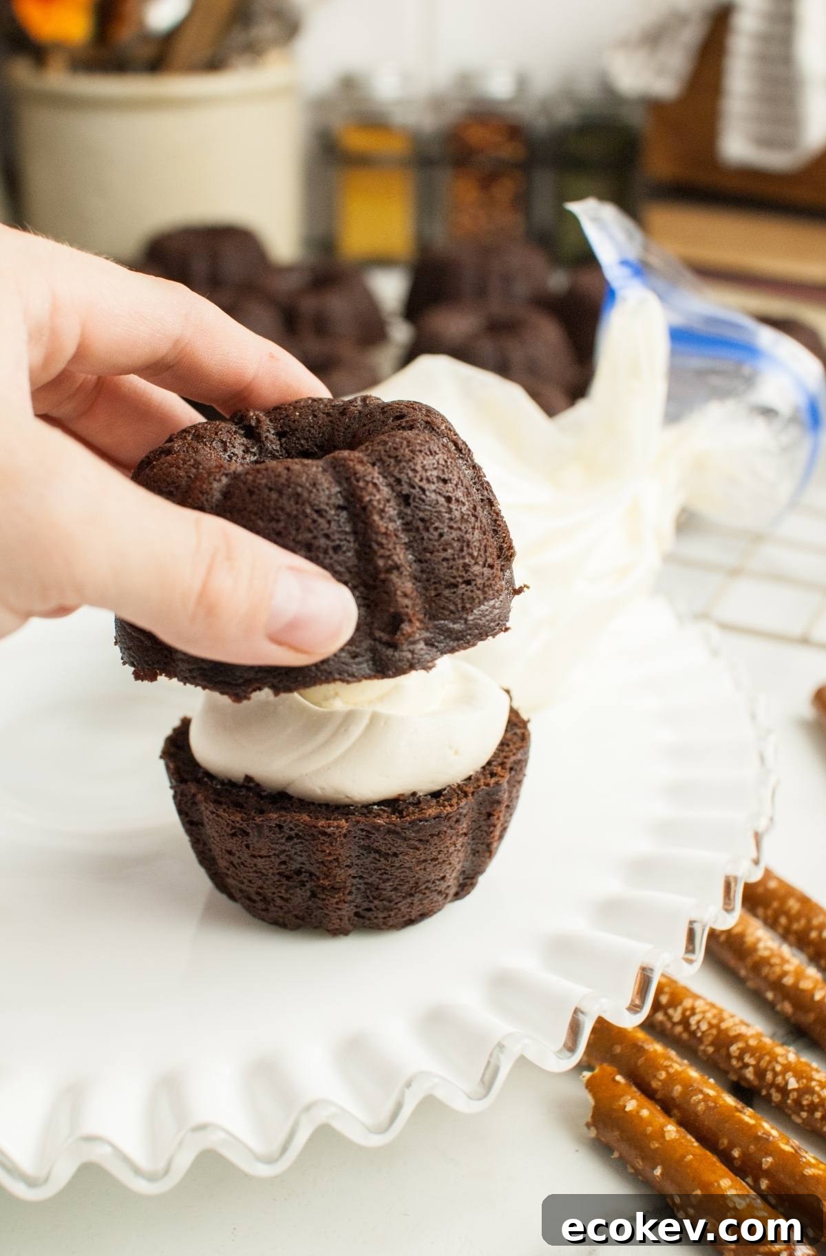 A hand places a Pumpkin Shaped Mini Bundt Cake with frosting filling on a white plate, making it a perfect Thanksgiving or Halloween dessert.