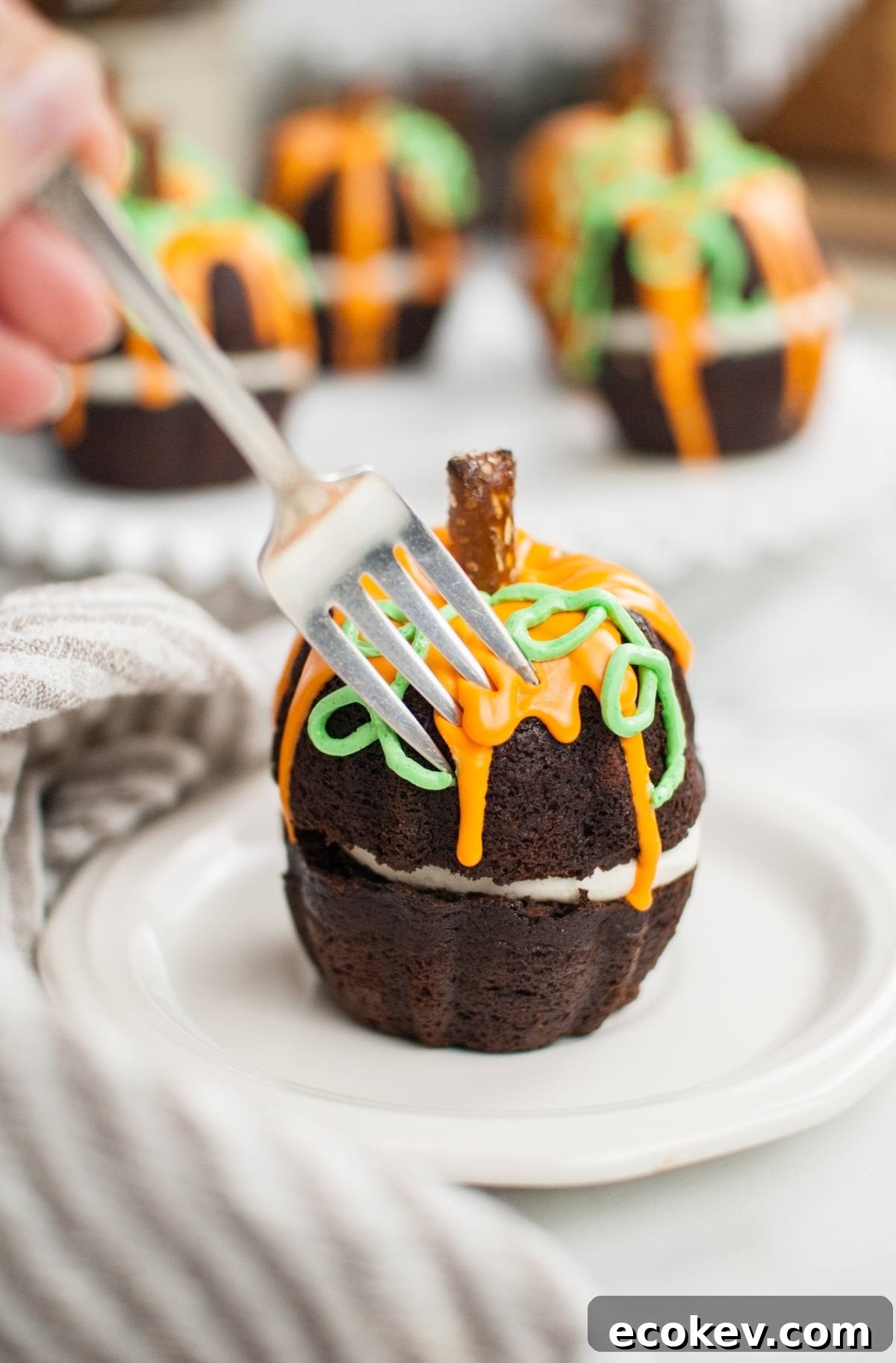 A fork cuts into a pumpkin bundt cake with orange and green icing, shaped like a festive Halloween pumpkin cake, served on a white plate.