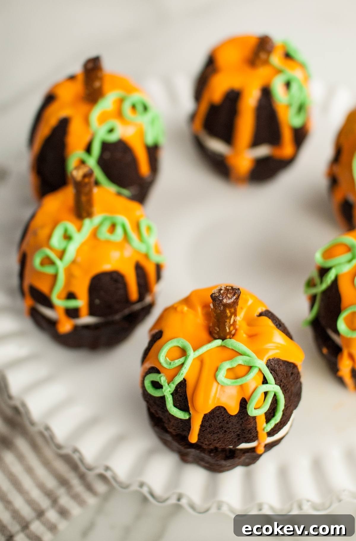 Chocolate cupcakes decorated as pumpkins with orange icing, green frosting vines, and pretzel stick stems—perfect as Halloween pumpkin cakes or a festive Thanksgiving or Halloween dessert.