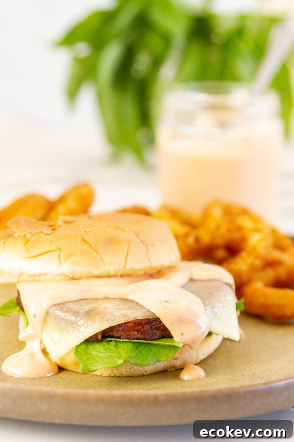 burger and onion rings served on a plate, a jar of sauce in the background.