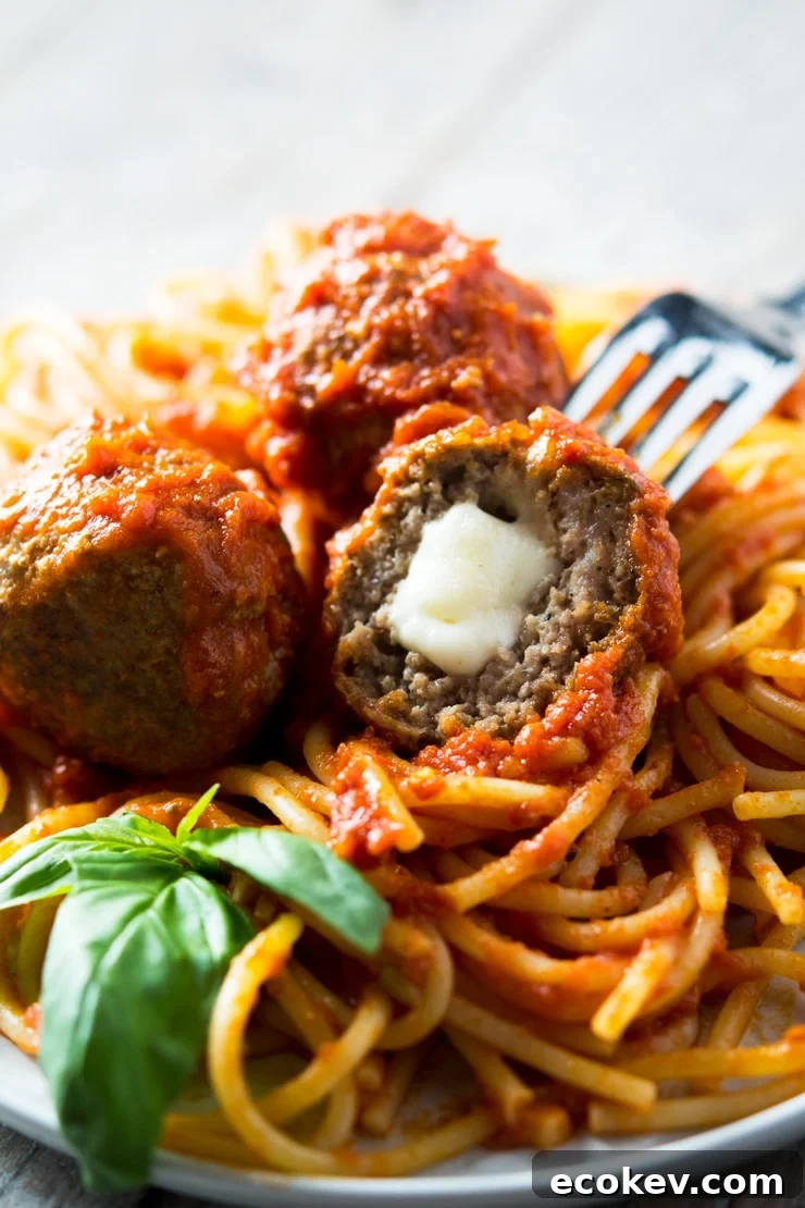 a close up of a mozzarella stuffed meatball on a fork in a plate of spaghetti