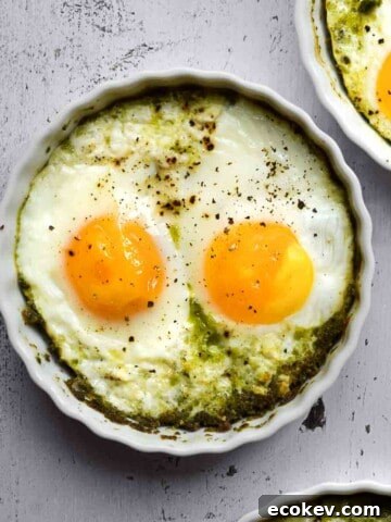 Overhead view of baked eggs in ramekins with pesto,