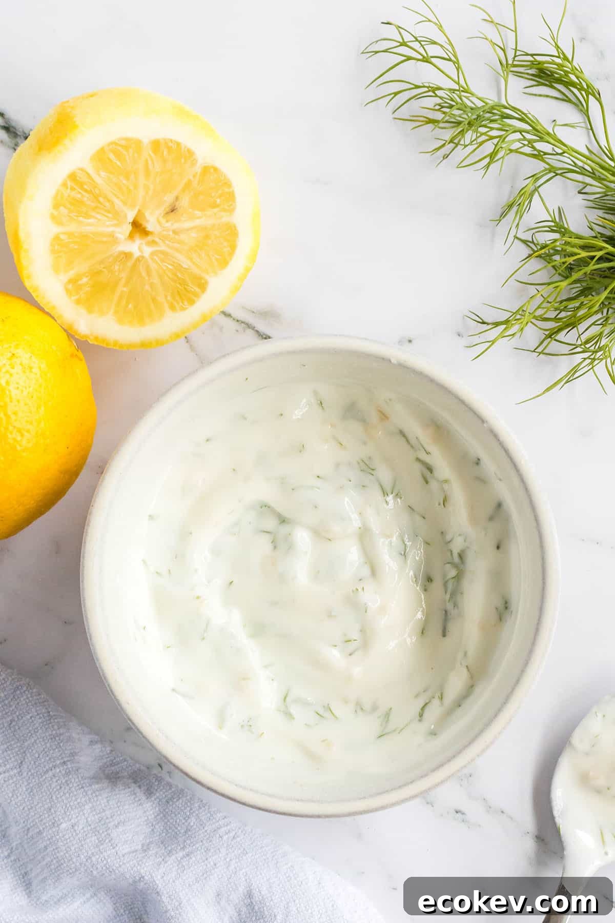 Blended lemon dill sauce in white bowl with sliced lemons on the side.