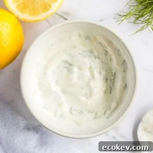 Blended lemon dill sauce in white bowl with sliced lemons on the side.