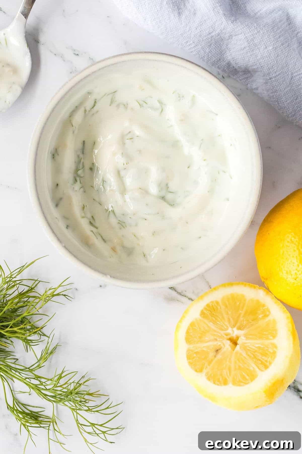 Lemon dill sauce in white bowl with sliced lemons on the side.