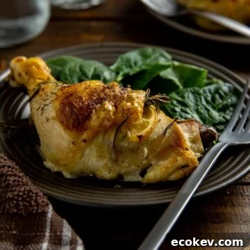 Baked chicken leg quarter on brown plate with fresh baby spinach on the side.