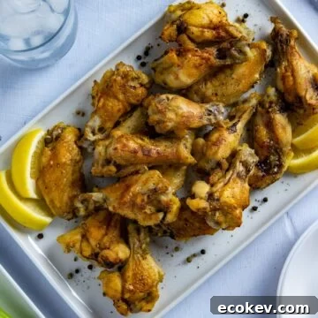 Baked chicken wings on white platter with lemon wedges.