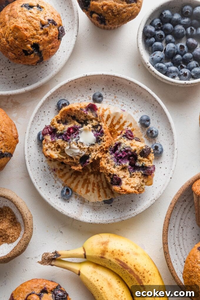 Countertop scattered with banana blueberry muffins, extra bananas and blueberries, and coarse sparkling sugar.