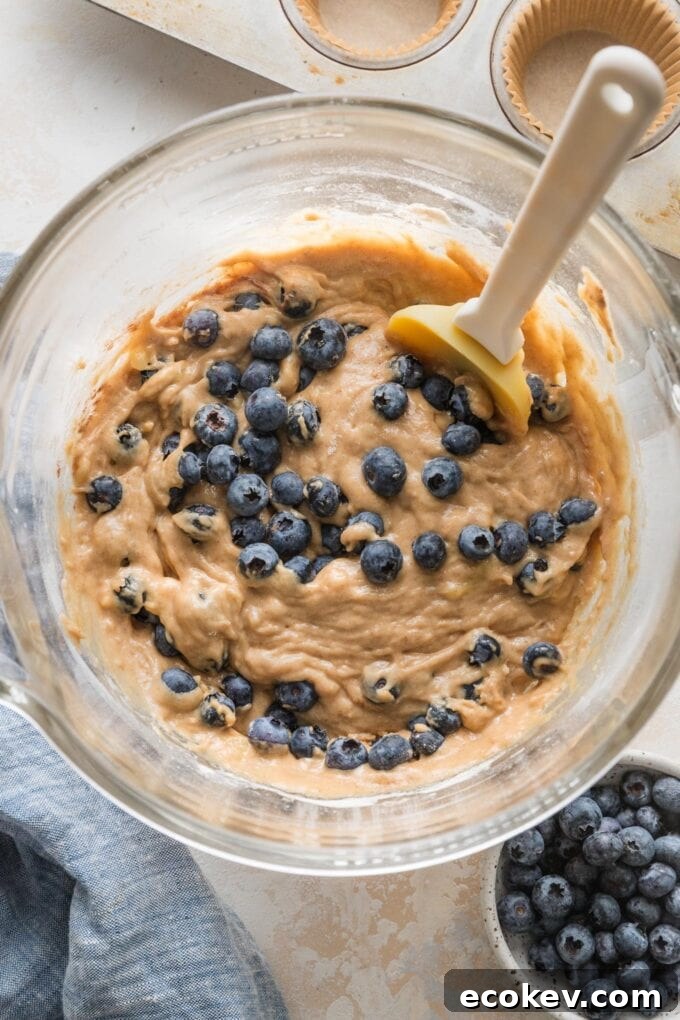 Close-up of a thick banana muffin batter with blueberries mixed in, in a clear glass mixing bowl.