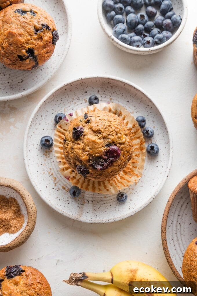 Overhead view of a banana blueberry muffin unwrapped from its liner and set on a small plate to eat.