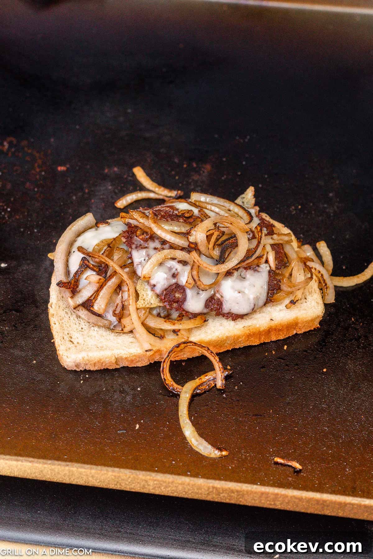 Slice of bread topped with ground beef patty and cooked slice onions on the griddle