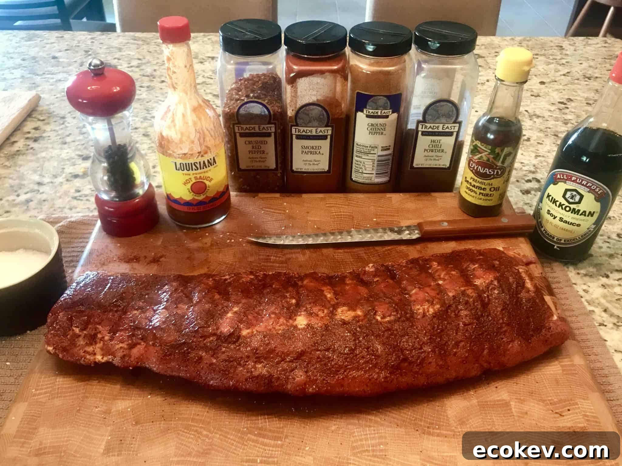 Rack of ribs on wooden cutting board with spices lined up behind it close up view