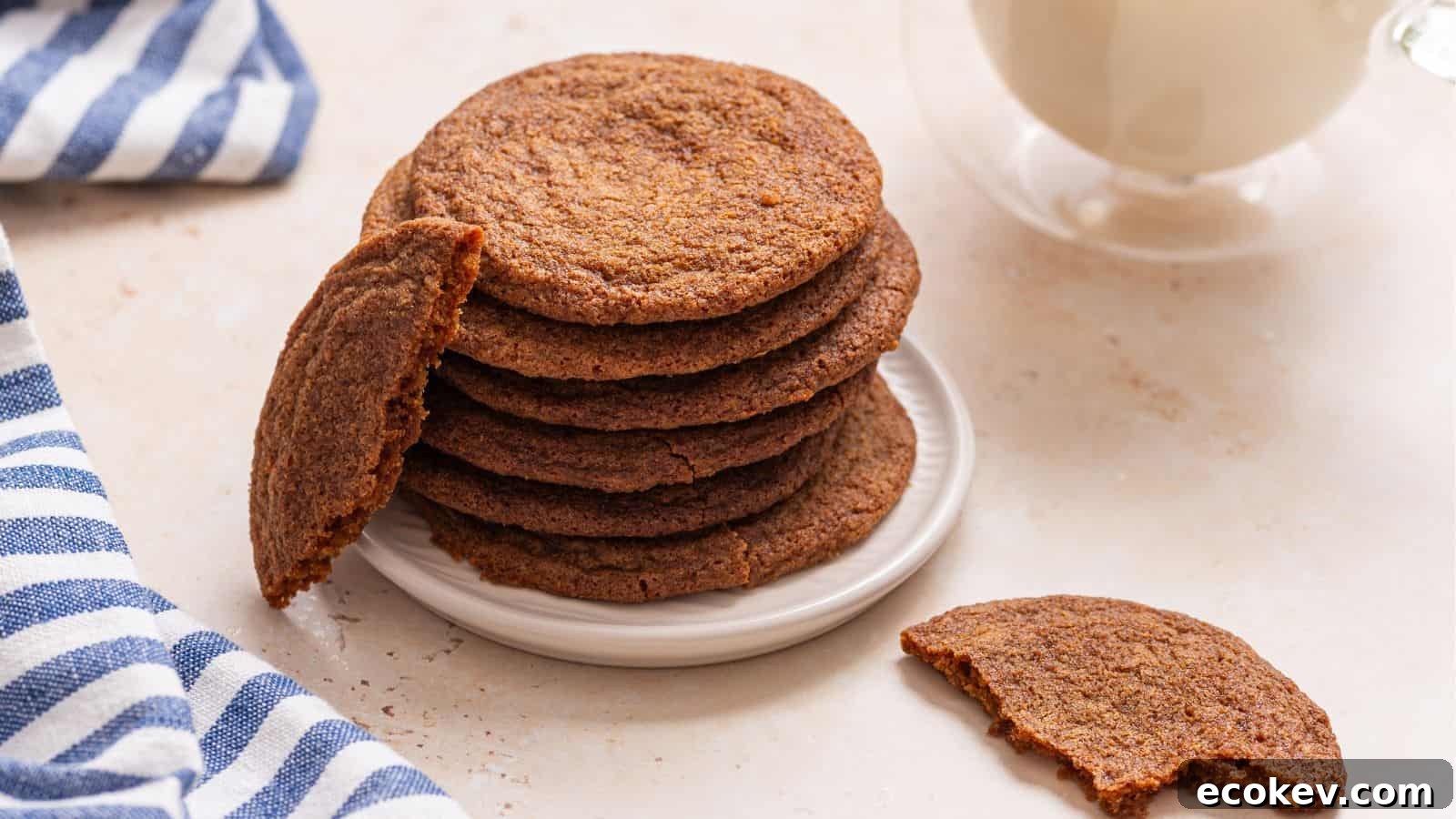 A stack of crisp brown sugar cookies on a plate with one cookie broken in half, accompanied by a glass of milk and a striped napkin.