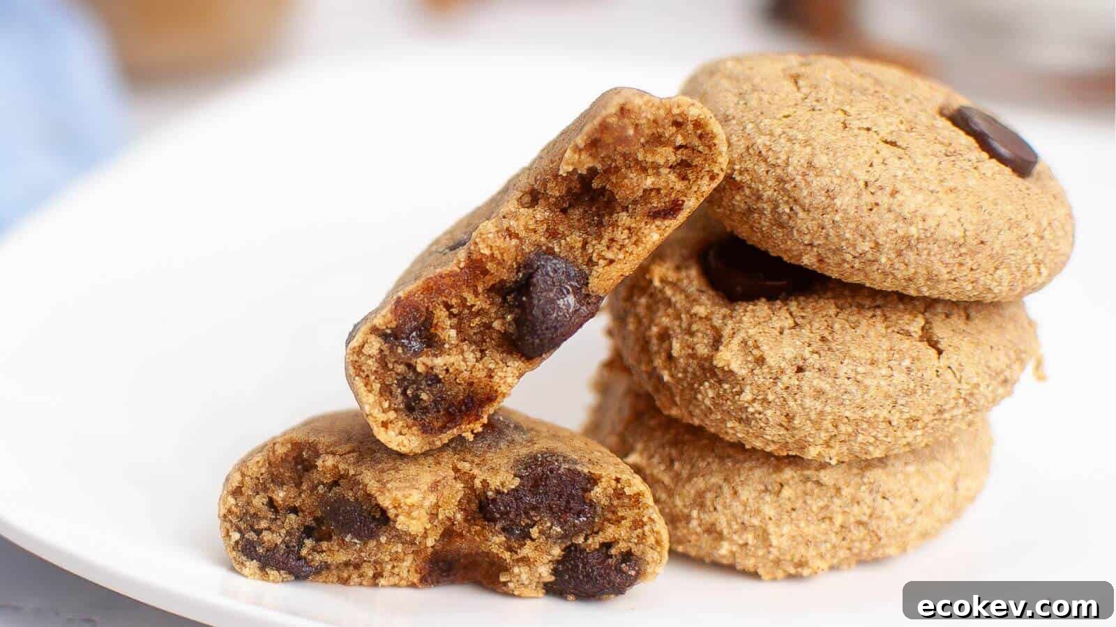 A stack of chocolate chip cookies on a white plate, with one cookie broken in half to show the chocolate chips inside.