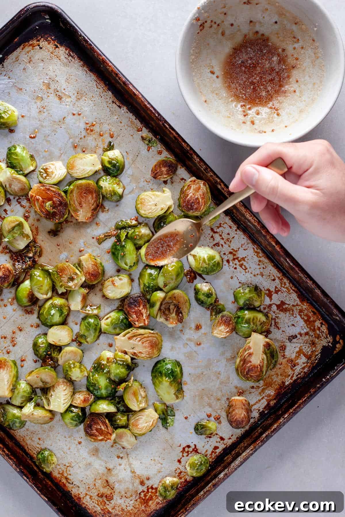 Roasted brussels sprouts get drizzled with maple balsamic vinegar sauce on a baking sheet.