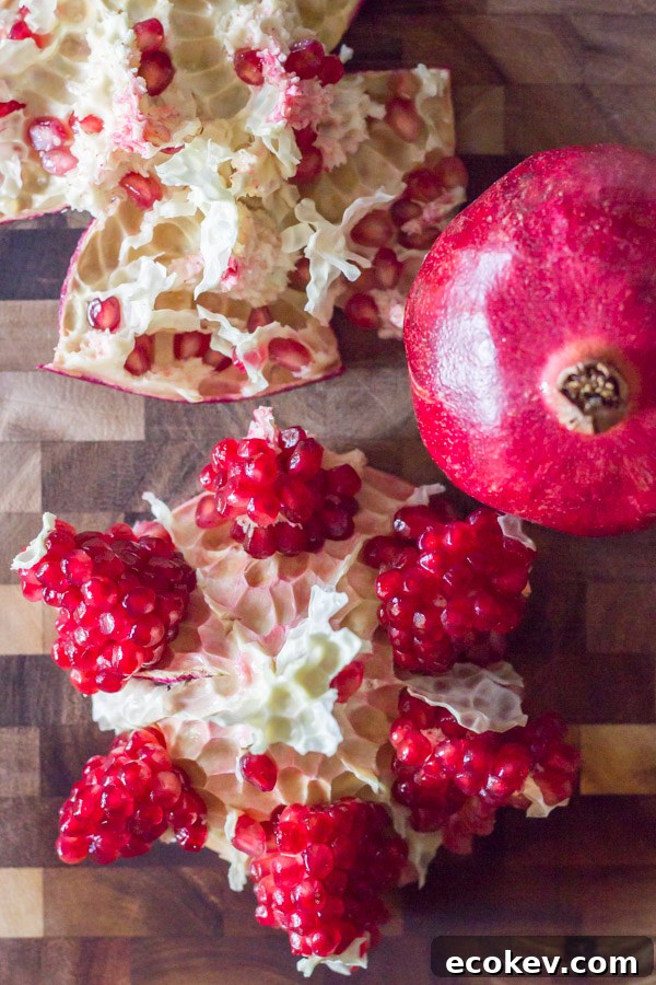A pomegranate cut open on a cutting board, sitting next to a whole pomegranate.