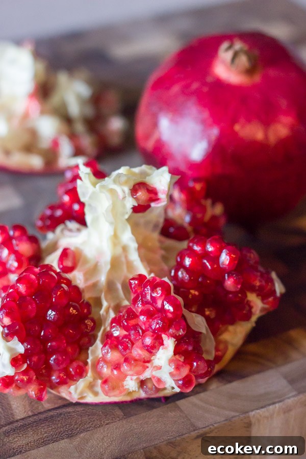 A pomegranate cut open on a cutting board, sitting next to a whole pomegranate.