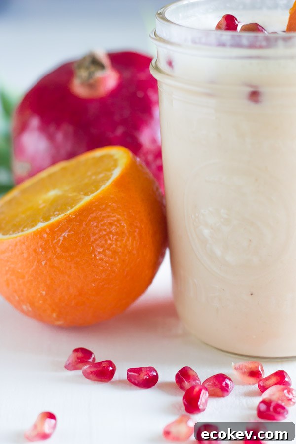 Pomegranate Citrus Smoothie in a glass jar with pomegranate seeds on top, with an orange and pomegranate next to the glass.