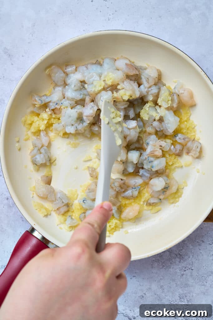 Chopped shrimp added into a skillet with sautéed onions and garlic.