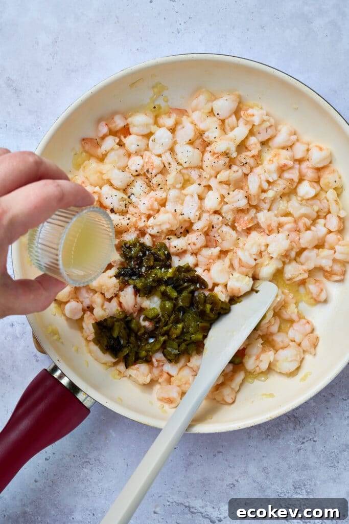 Pouring lime juice into a skillet with sautéed shrimp and chopped, roasted poblano peppers