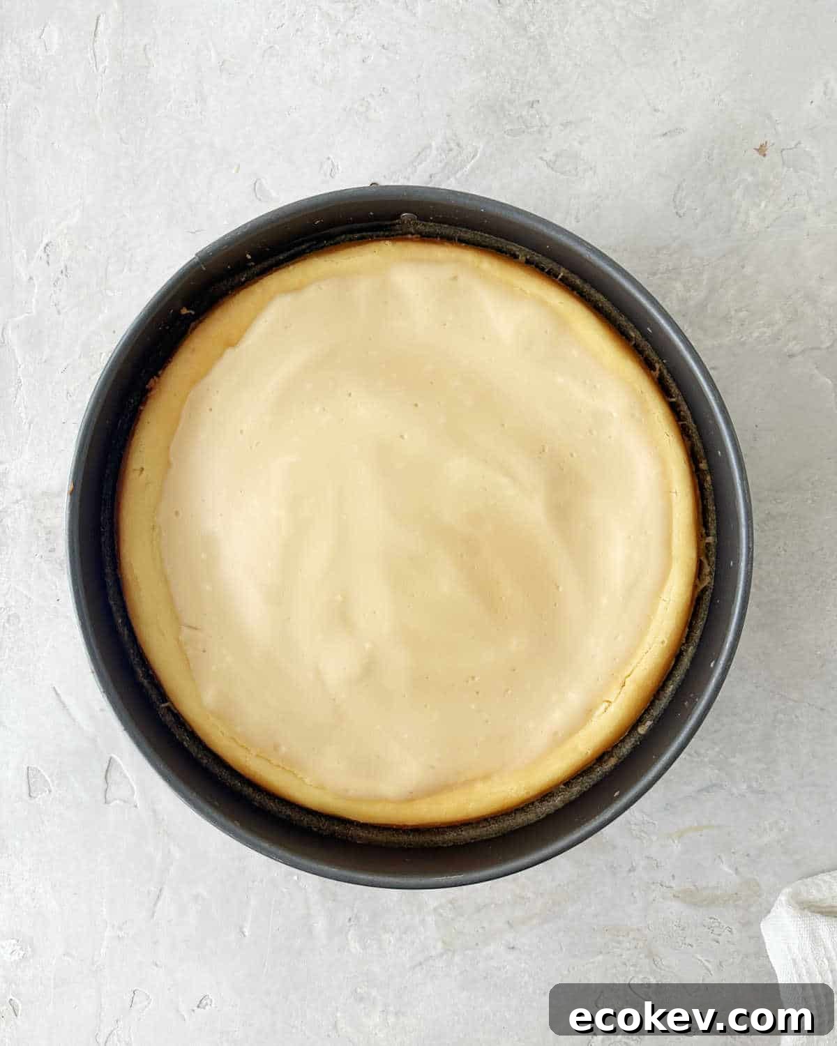 Baked Baileys cheesecake with sour cream topping on a metal pan. Light grey surface.