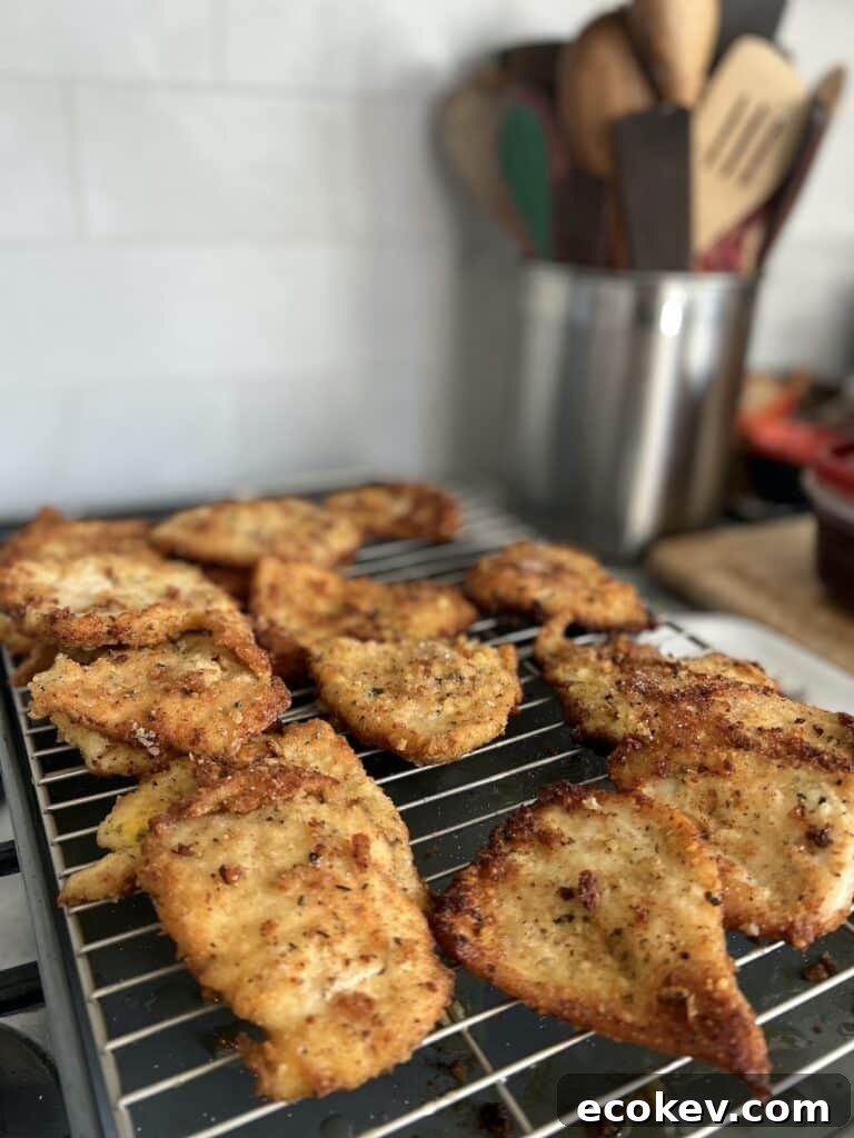 Finished batch of Italian chicken cutlets on rack over sheet pan with utensil canister in the background.
