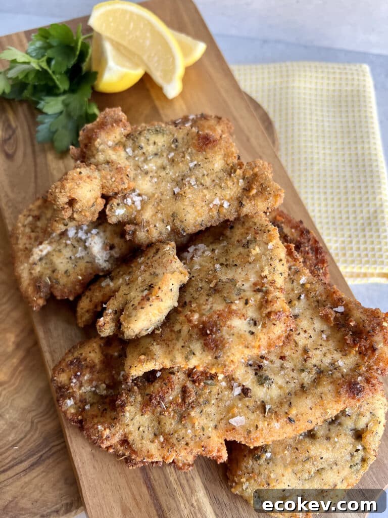 Italian Chicken Cutlets on wooden serving board with lemon wedge and parsley garnish.