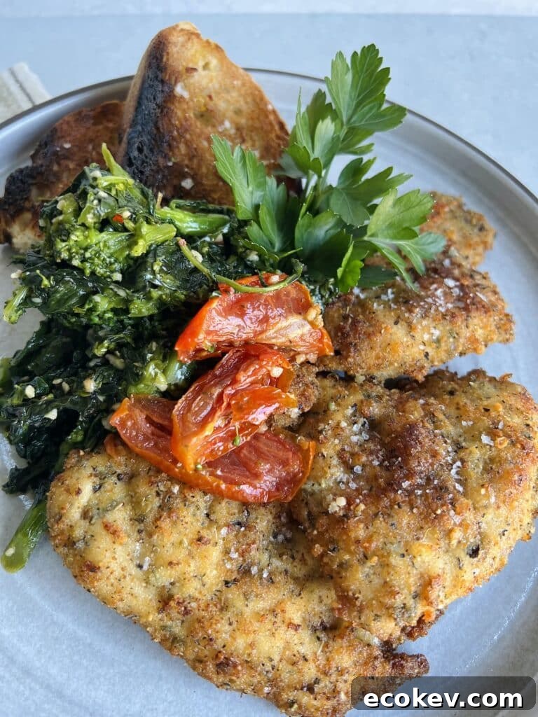 Italian Chicken Cutlets on plate with roasted tomatoes, broccoli rabe, toasted bread and parsley garnish.