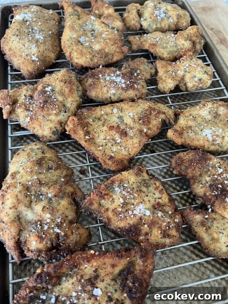 Finished batch of Italian chicken cutlets sprinkled with salt flakes on rack over sheet pan.