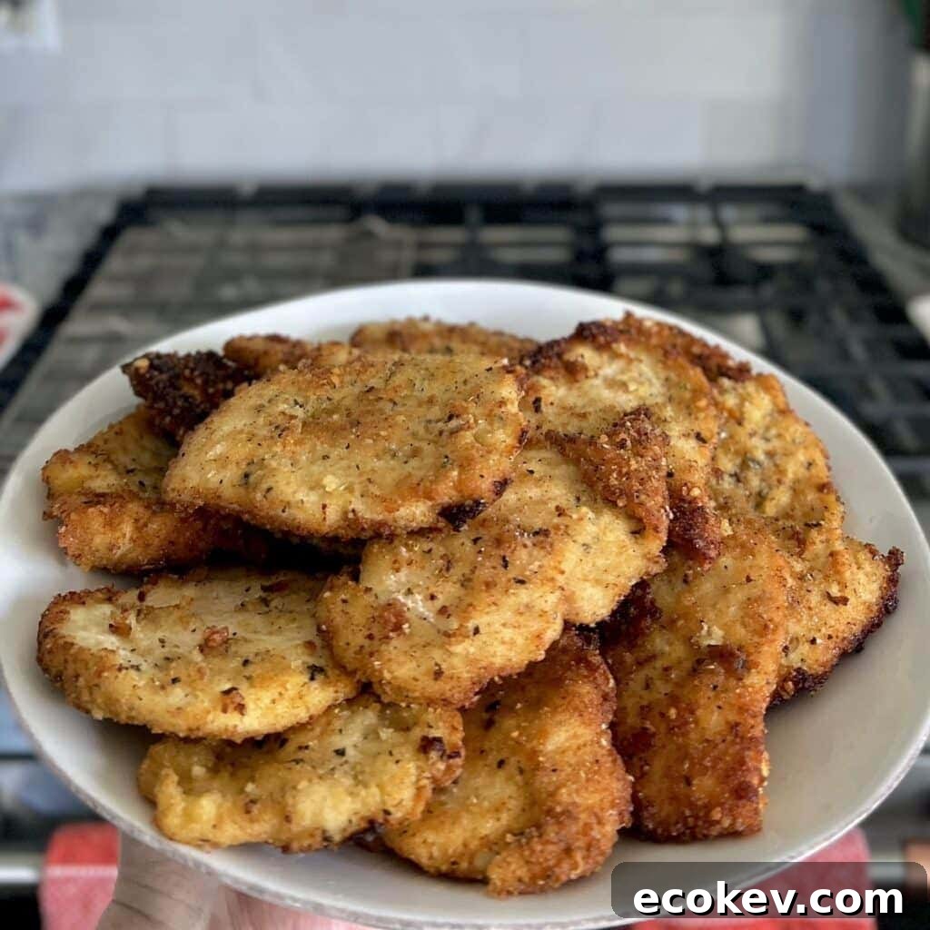 Italian Chicken Cutlets on a white plate with stove in background.