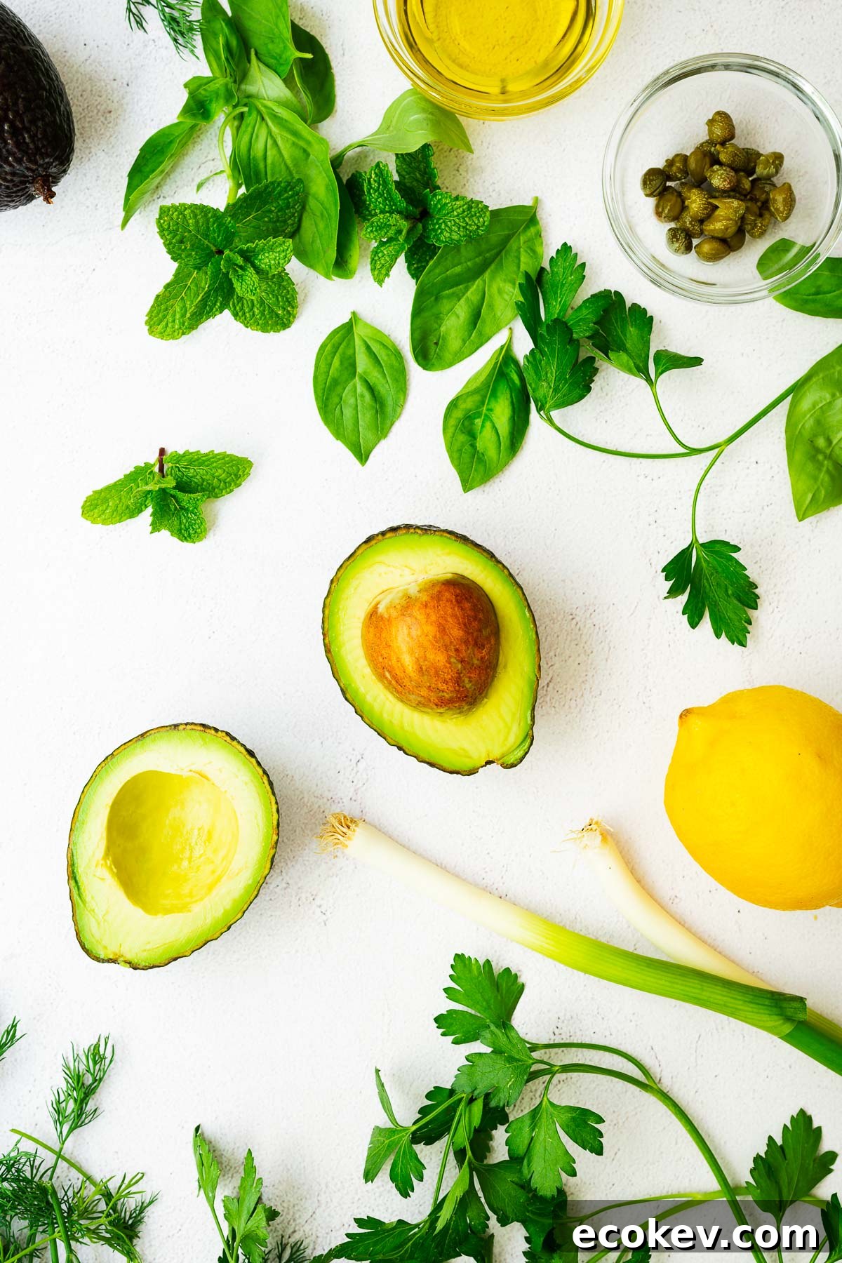 Ingredients for an avocado green goddess dressing on a light concrete surface.