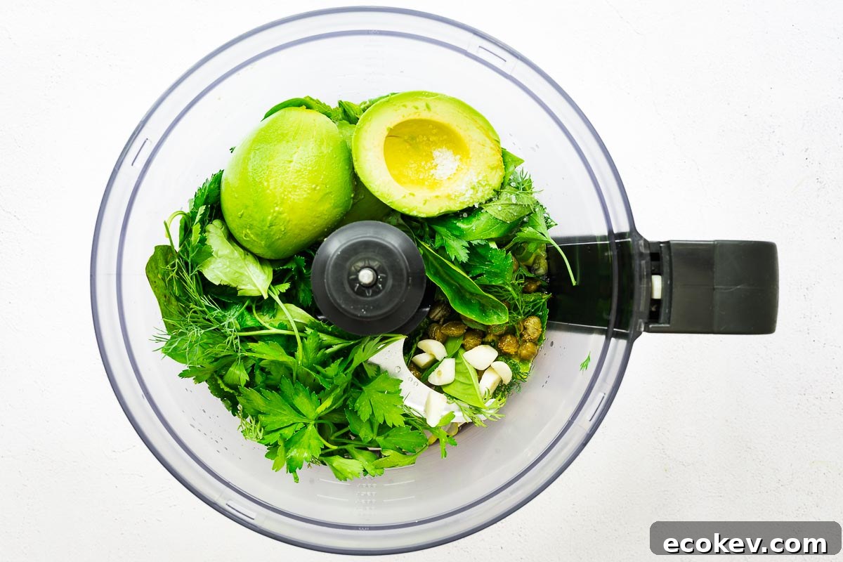 Ingredients for an avocado green goddess sauce in the bowl of a food processor viewed from above.