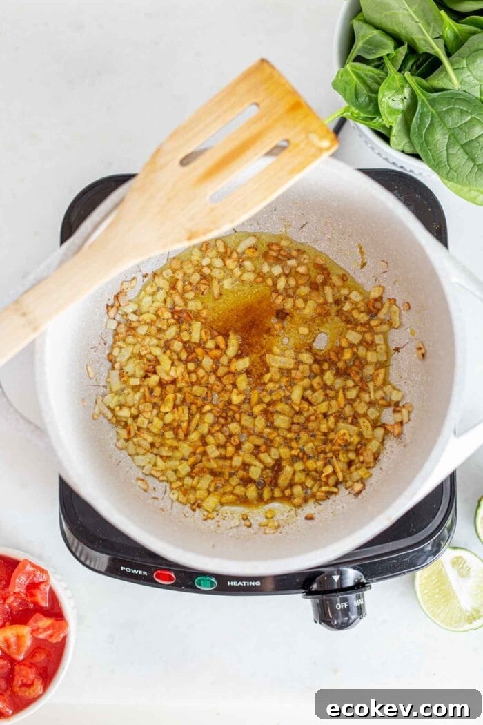 Spices, onions, garlic and ginger cooking in a pot with a wooden spoon.