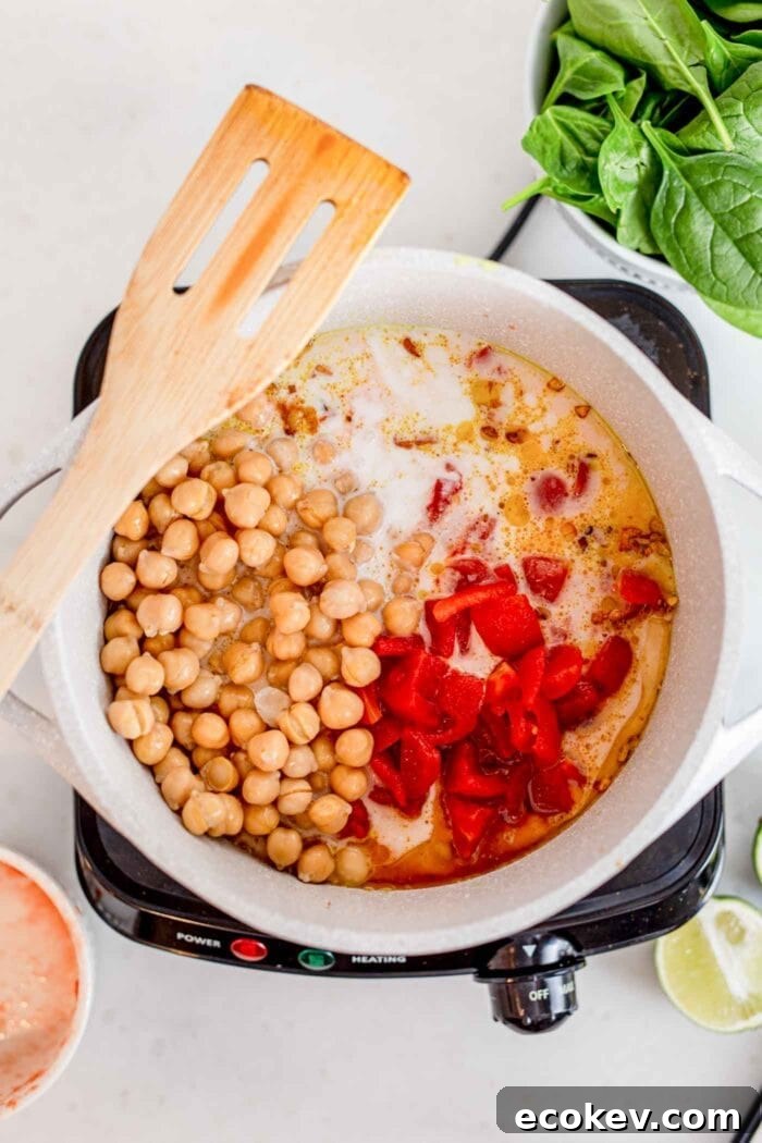 Diced tomato, rice, coconut milk and chickpeas cooking in a pot with a wooden spoon.