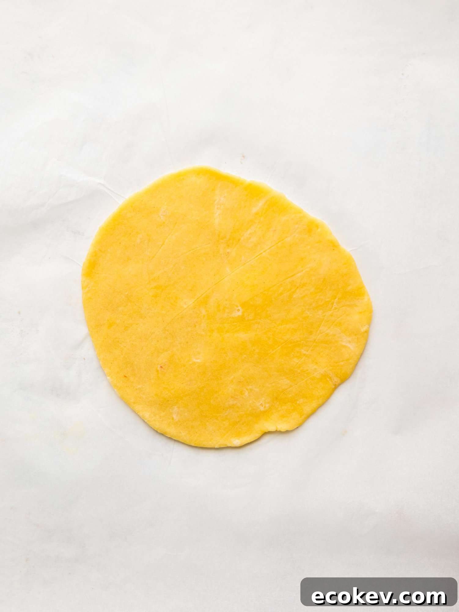 An empanada disk on a sheet of parchment paper.
