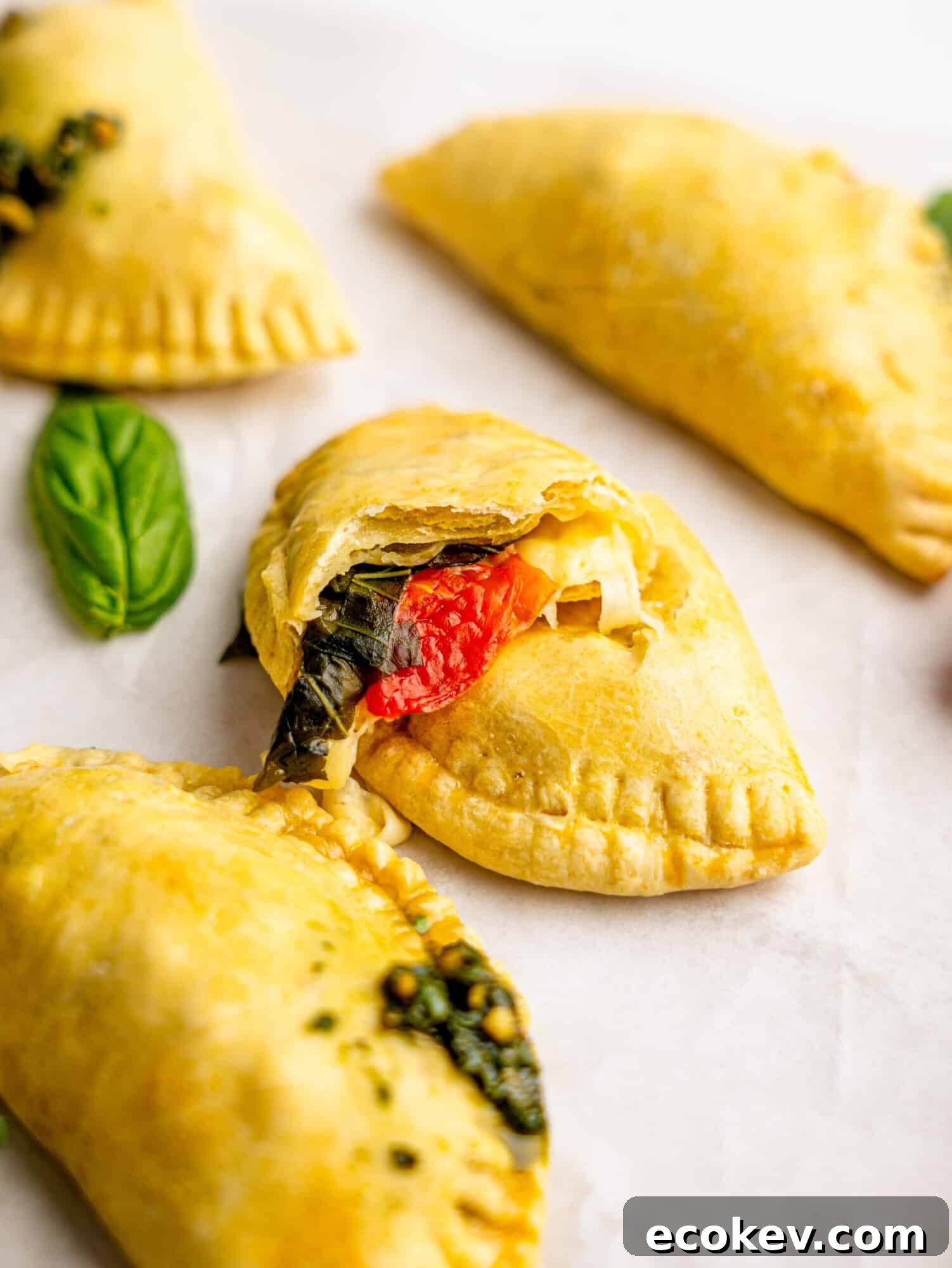 A caprese empanada torn in half revealing melted mozzarella, tomatoes and basil.