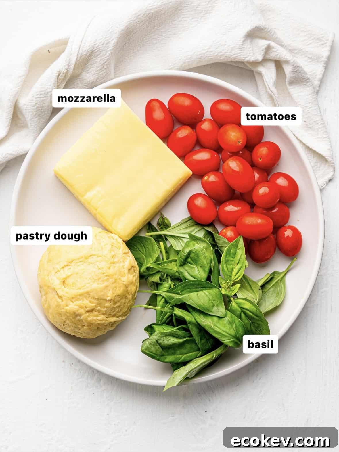 Empanada dough, mozzarella, basil and tomatoes on a white plate.