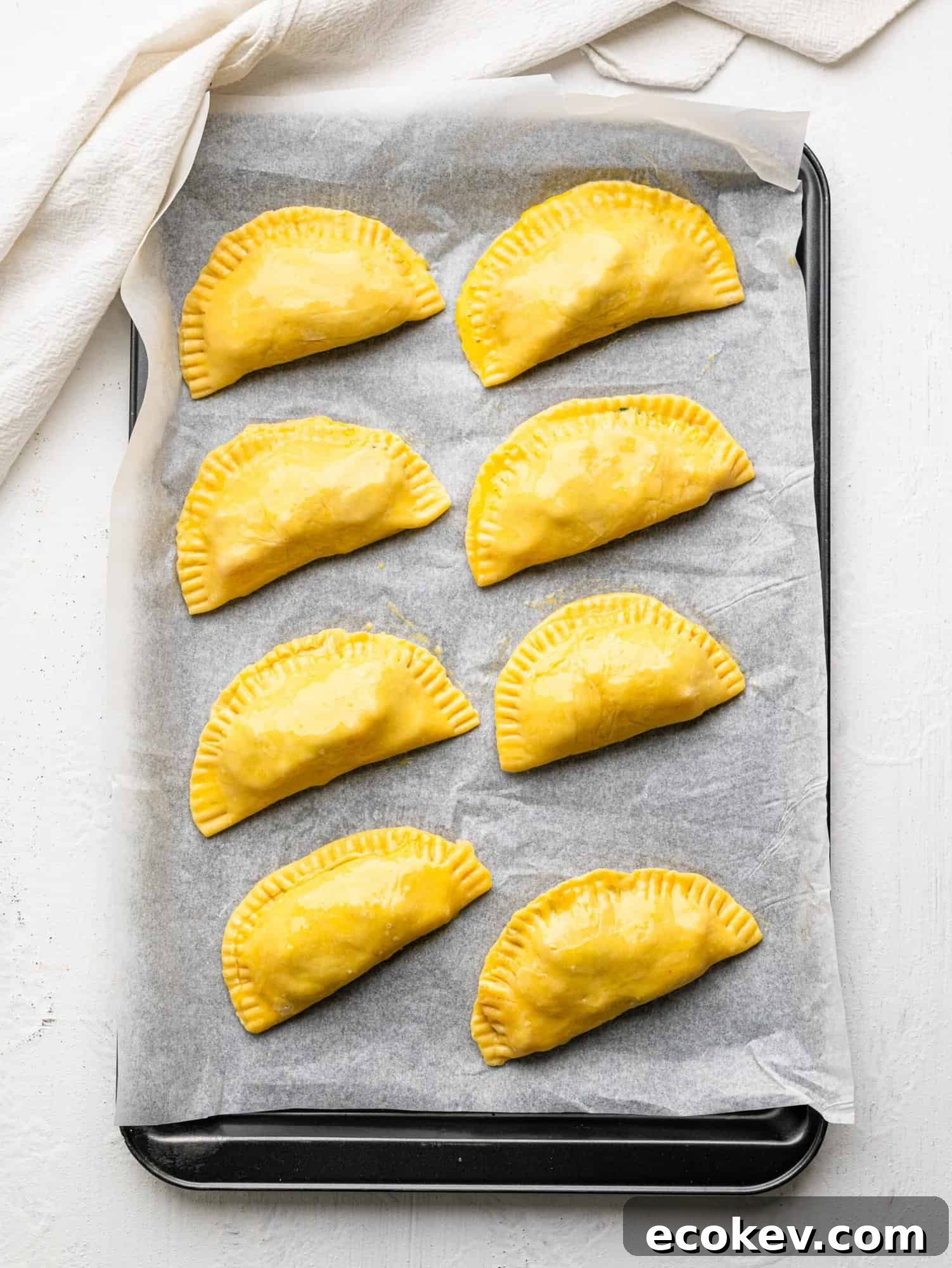 Eight caprese empanadas on a baking sheet before being baked.