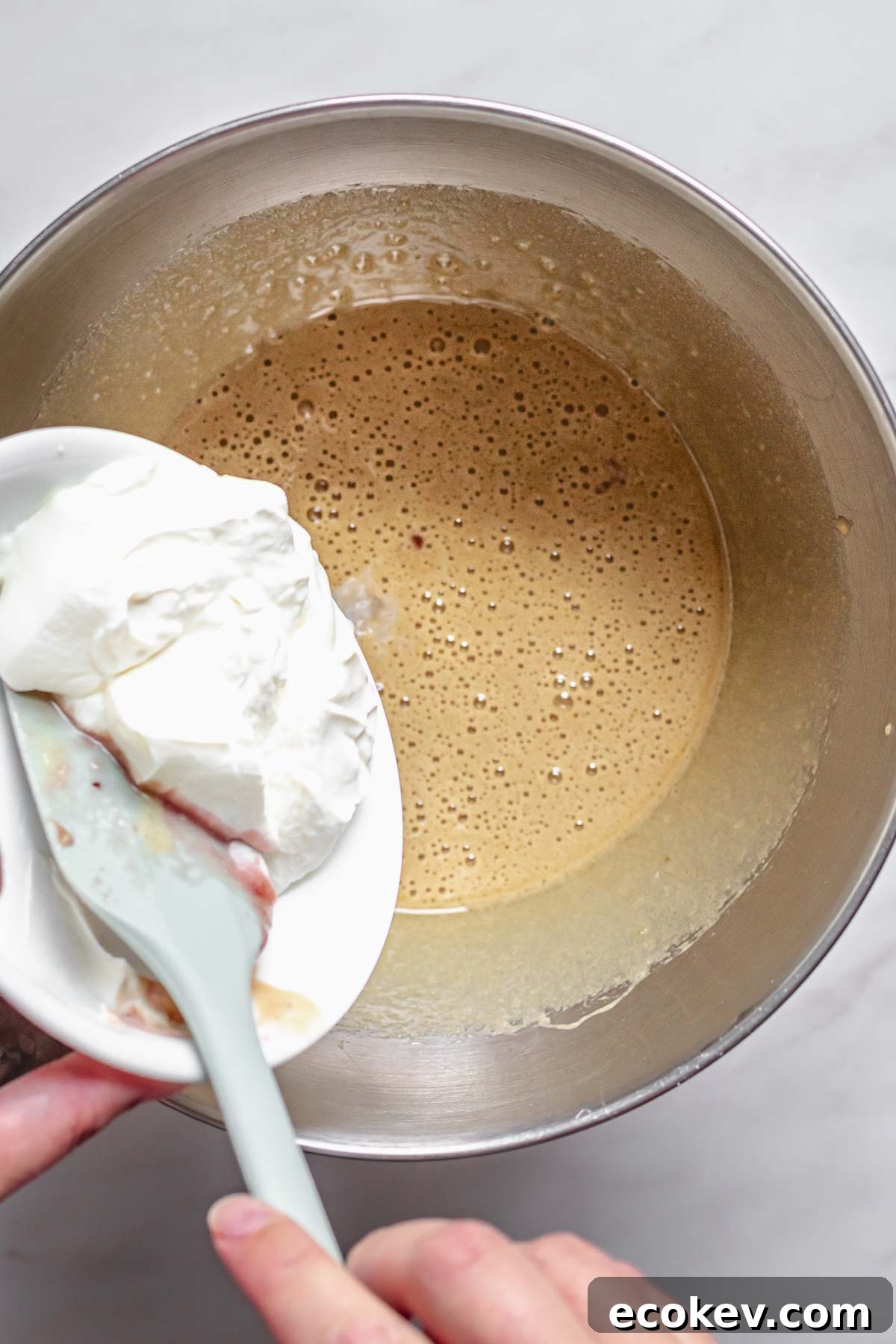 Sour cream being added to wet cake batter.