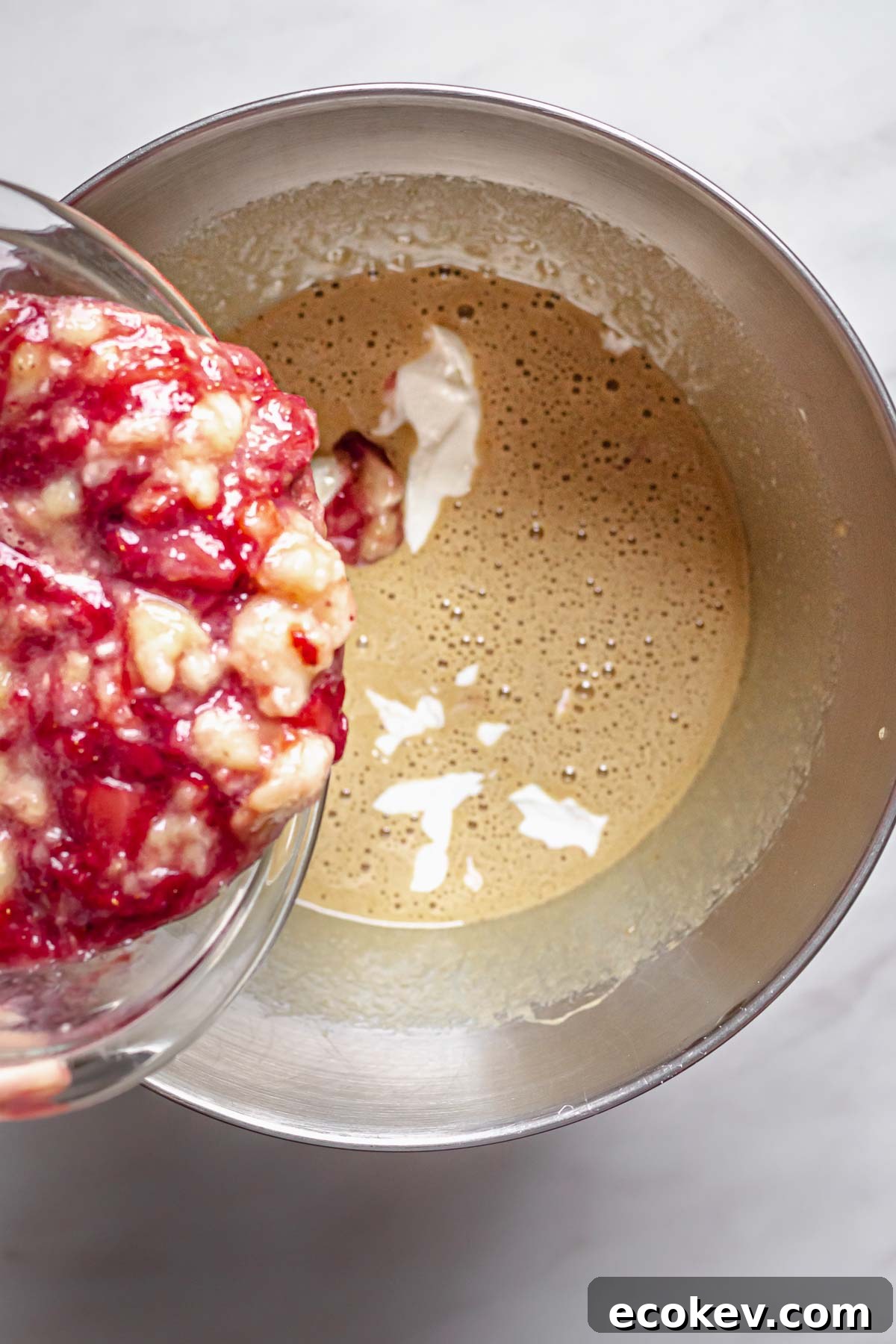 Mashed strawberries and bananas pouring into cake batter.