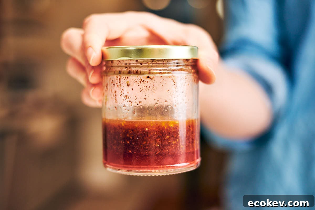 A hand holding a glass jar of sumac vinaigrette.