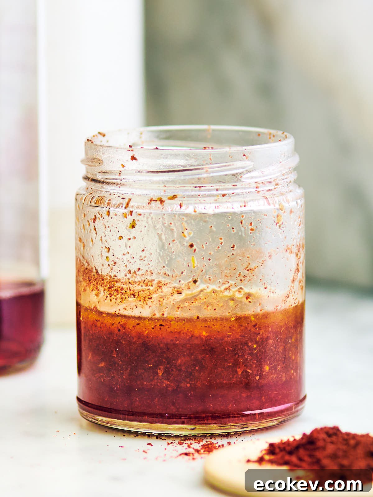 Sumac dressing and dried sumac on a marble kitchen counter.