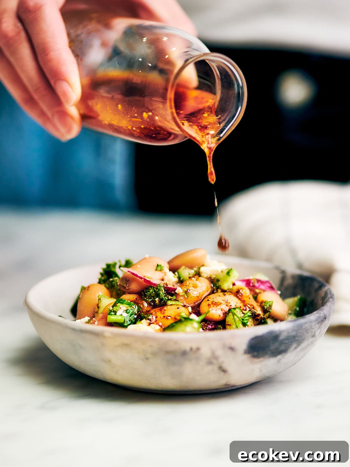 Sumac dressing being poured over a bowl of Butter Bean Salad.